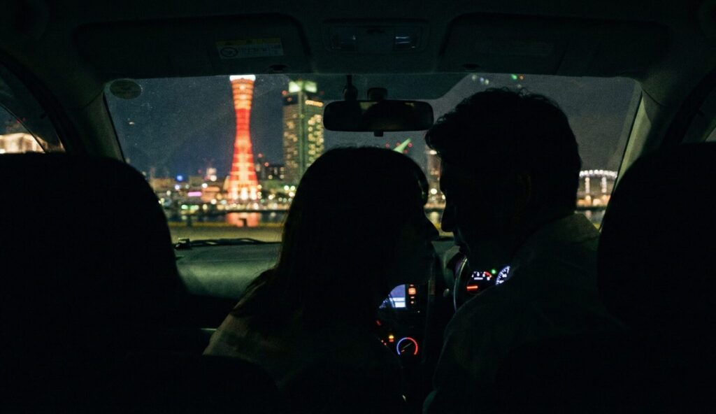 夜の神戸ハーバーランドの駐車場で、ポートタワーの夜景を前に、車内で親密に過ごす夫と浮気相手のシルエット。