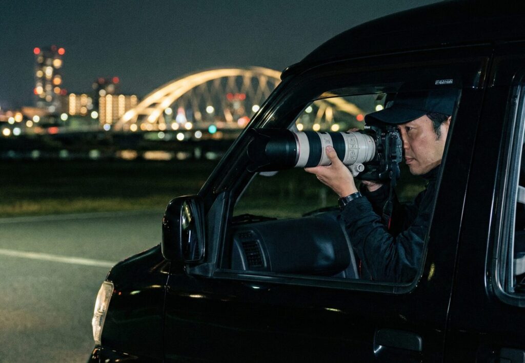 RESTART探偵事務所の調査員チームが、此花区（舞洲やUSJ周辺）にて、特殊な望遠カメラと無線機を駆使し、連携して尾行・張り込みを行っているプロフェッショナルな様子。