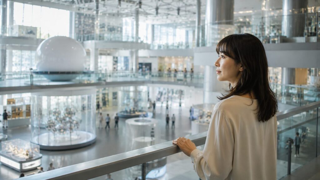 近未来的な科学館の展示ホールで複数の展示エリアを見渡す日本人女性。婚前調査で確認できる内容と確認できない内容を正しく理解し、冷静に判断する重要性を象徴的に表現した写真風イメージ。婚前調査の範囲を解説する記事用見出し画像。