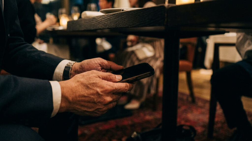 レストランでメッセージ通知が来たスマートフォンを慌てて伏せる男性の手元