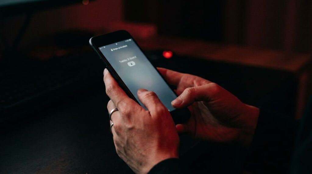暗がりの中で他人のスマートフォンに手を伸ばそうとするプライバシー侵害リスクのイメージ